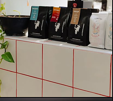 Bolsas de café Hyperjump con la mascota astronauta, en el anaquel de una cafetería socia